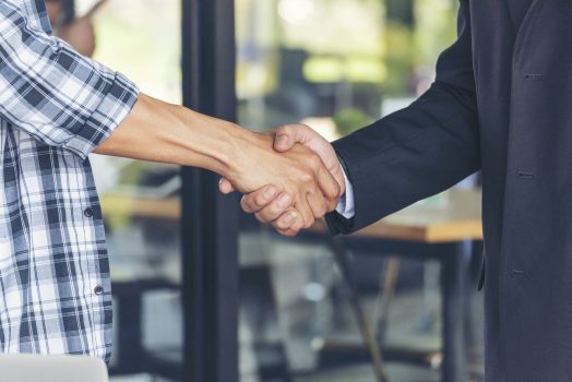 Diversity two business partners shaking hands together with business contract mergers and acquisitions. Close up honest hands business teams handshaking at office desk. Trust partnership shaking hands